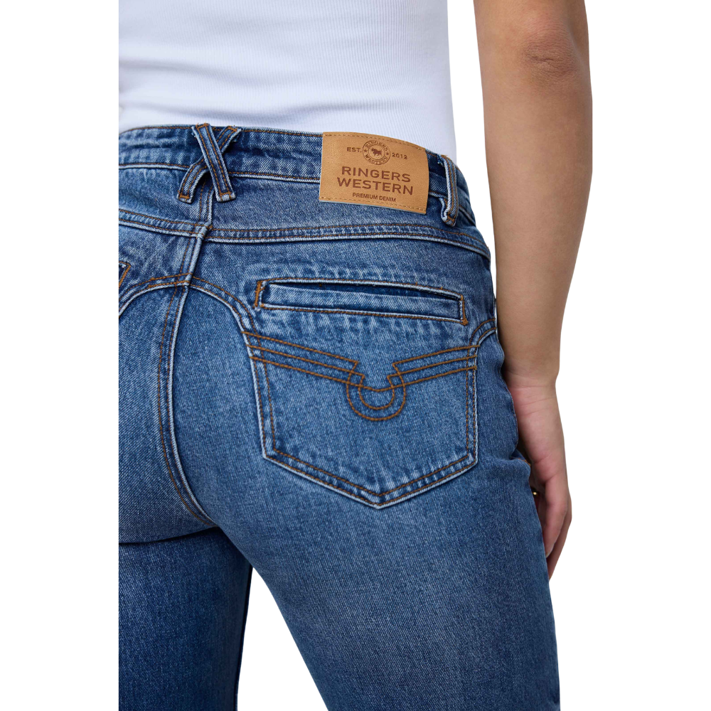 Close-up back view of a person wearing blue denim jeans with a tan leather Ringers Western waistband patch and a white top visible at the waist.