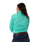 A woman with long dark hair with her back to the camera, wearing a Ringers Western Womens Pentecost River Half Button Work Shirt in Mint and blue jeans with a brown belt. The background is plain white.