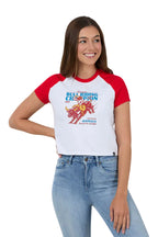 A woman modeling a white and red raglan t-shirt with a colorful bull riding graphic on the front, paired with light blue jeans, against a solid white background.