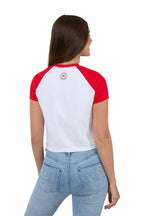 Woman wearing a red and white baseball-style shirt with a logo on the back, standing against a white background.