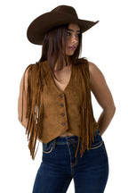 A woman wearing a brown suede fringe vest, a matching brown cowboy hat, and blue jeans, photographed against a white studio background.
