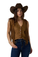 A woman modeling a brown suede fringe vest, dark brown cowboy hat, and dark blue jeans against a white studio background.