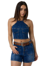 A woman modeling a matching blue denim halter crop top and shorts set with a brown belt, photographed against a white studio background.
