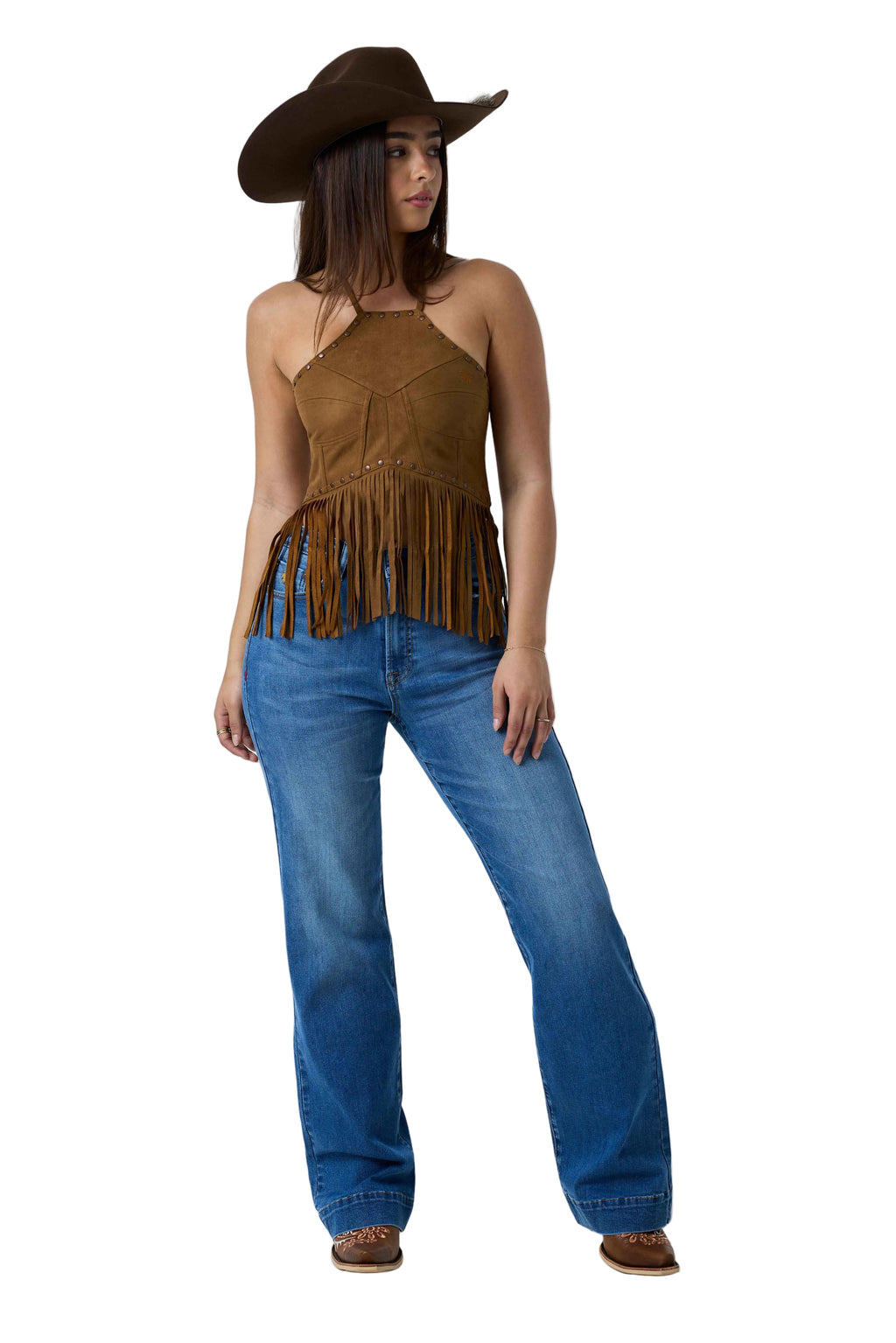 A woman modeling a brown suede halter top with fringe, blue jeans, and a brown cowboy hat against a white studio background.