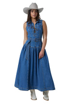 A woman modeling a sleeveless blue denim midi dress with a tie-front detail, matching belt, and flared skirt, styled with a light gray cowboy hat and white cowboy boots against a white studio background.