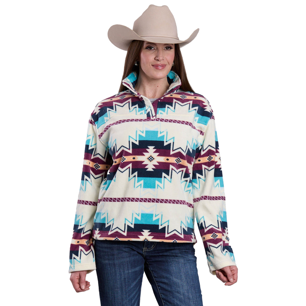 A woman in a beige cowboy hat, blue jeans, and the Roper Womens L/S Pullover (98250706) Multi—featuring teal, burgundy, and white geometric designs—stands smiling at the camera.