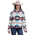 A woman in a beige cowboy hat, blue jeans, and the Roper Womens L/S Pullover (98250706) Multi—featuring teal, burgundy, and white geometric designs—stands smiling at the camera.