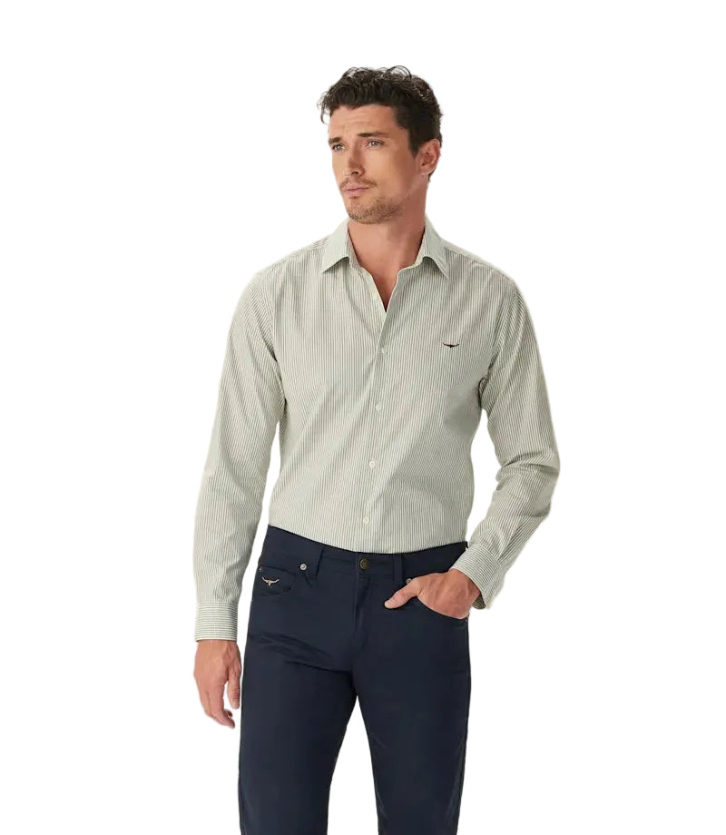 A man wears the R.M.Williams Mens Newland Poplin Check L/S Shirt in Moss with dark trousers, standing against a plain white background and looking to the side.