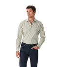 A man wears the R.M.Williams Mens Newland Poplin Check L/S Shirt in Moss with dark trousers, standing against a plain white background and looking to the side.