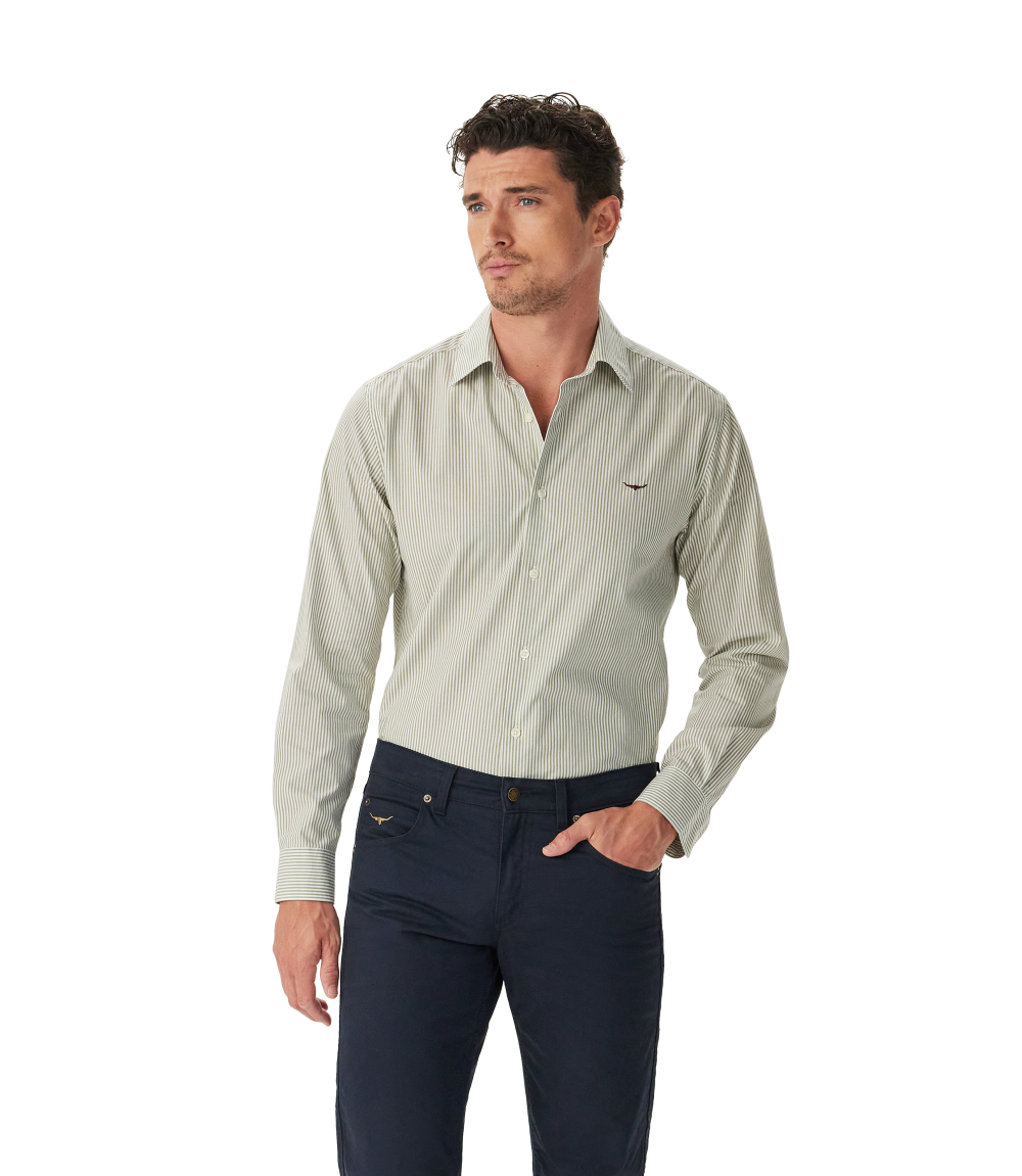 A man wears the R.M.Williams Mens Sommers Poplin Stripe L/S Shirt (SH200PM01) in white and green stripe, standing against a plain white background with one hand in his pocket and looking slightly to the side.