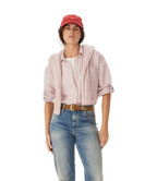 A woman in an R.M.Williams Womens Hopeland Linen Check L/S Shirt (Ice Pink), white top, blue jeans with a brown belt, and a red cap stands against a plain white background.