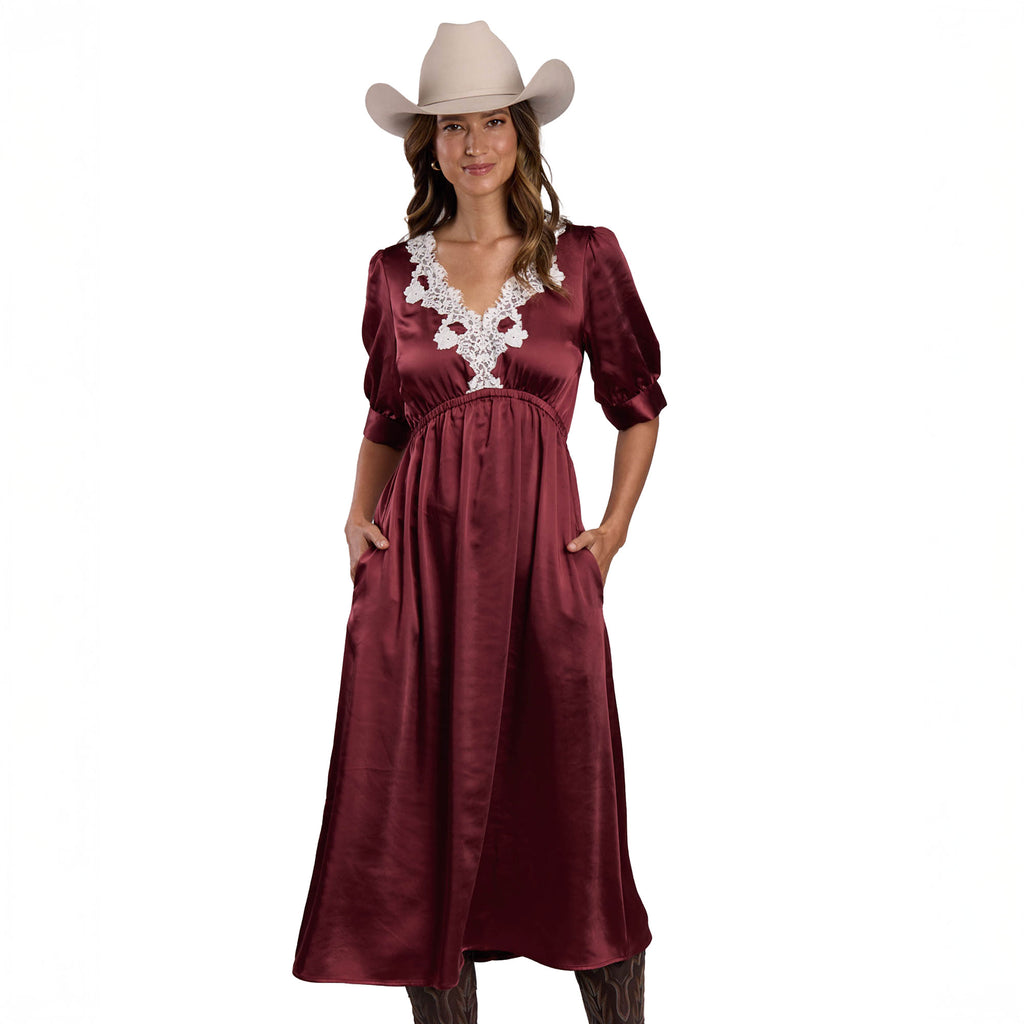 A woman wearing the Stetson Womens Collection S/S Dress (57565006) Solid Brown by Stetson and a beige cowboy hat stands with her hands in her dress pockets against a white background.