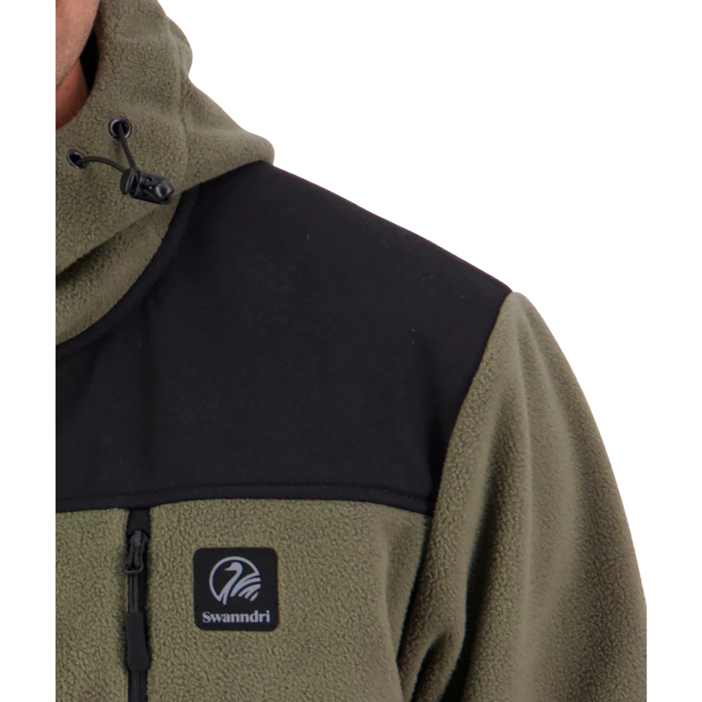 A man stands against a white background, wearing the Swanndri Men's High Rock Stormshield Jacket (SW2562070M) in Forest, an olive green weatherproof fleece with black yoke and lower back
