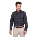 A man wears a Thomas Cook Mens Adam L/S Shirt (T6W1115034) in navy/tan, featuring cotton checks and a pen holder, tucked into light beige pants with a brown belt, standing against a plain white background.