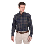 A man wears a Thomas Cook Mens Adam L/S Shirt (T6W1115034) in navy/tan, featuring cotton checks and a pen holder, tucked into light beige pants with a brown belt, standing against a plain white background.