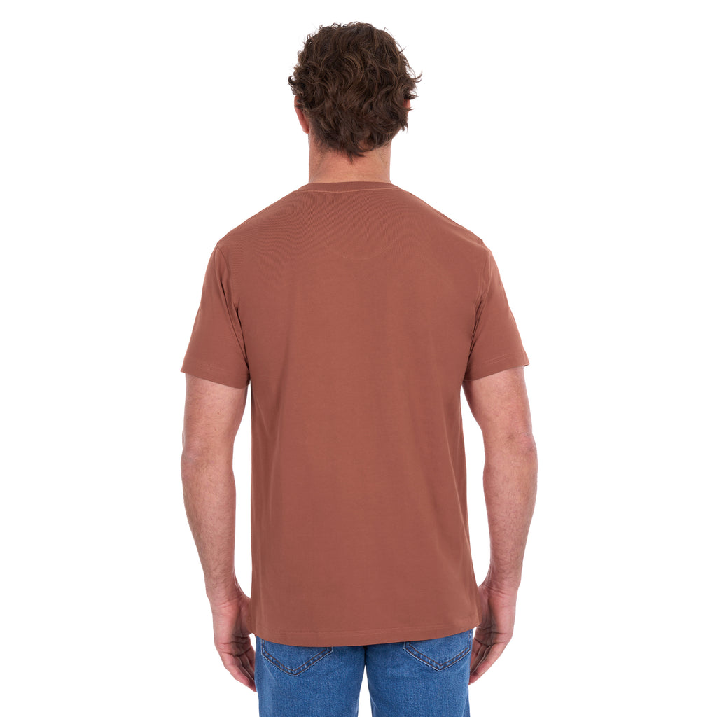 A man viewed from behind modelling a rust Thomas Cook Men's Classic Fit Short Sleeve Tee (TCP1514051) paired with blue denim jeans on a white background.