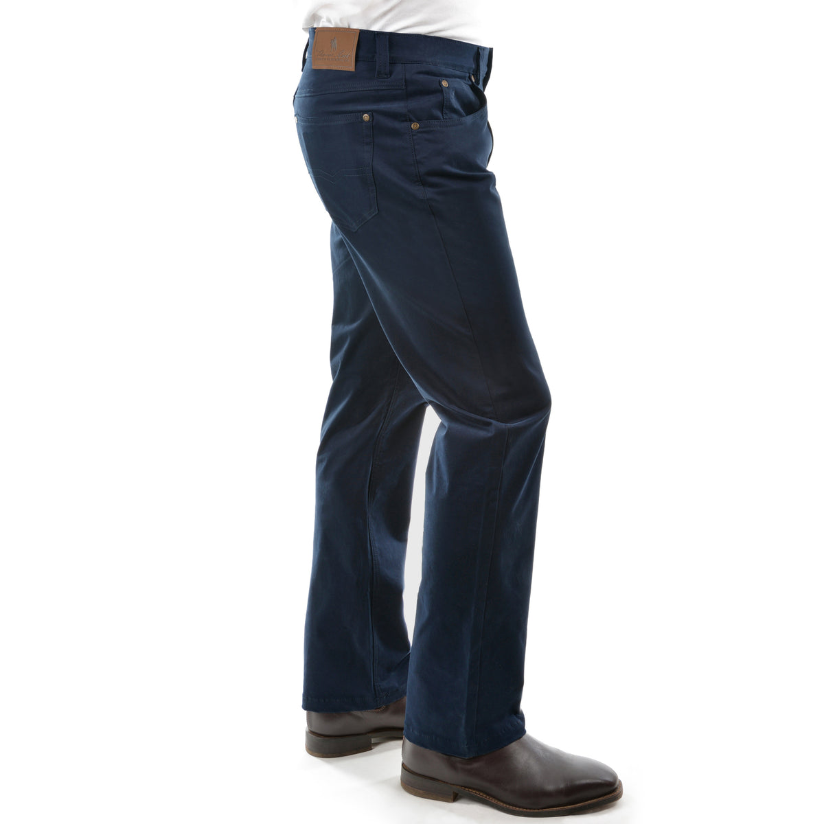 A pair of dark navy Thomas Cook Men's Jake Comfort Waist Jeans (TCP1215031) shown from the side on a model from the waist down, paired with a white shirt and dark brown leather boots, against a plain white background.