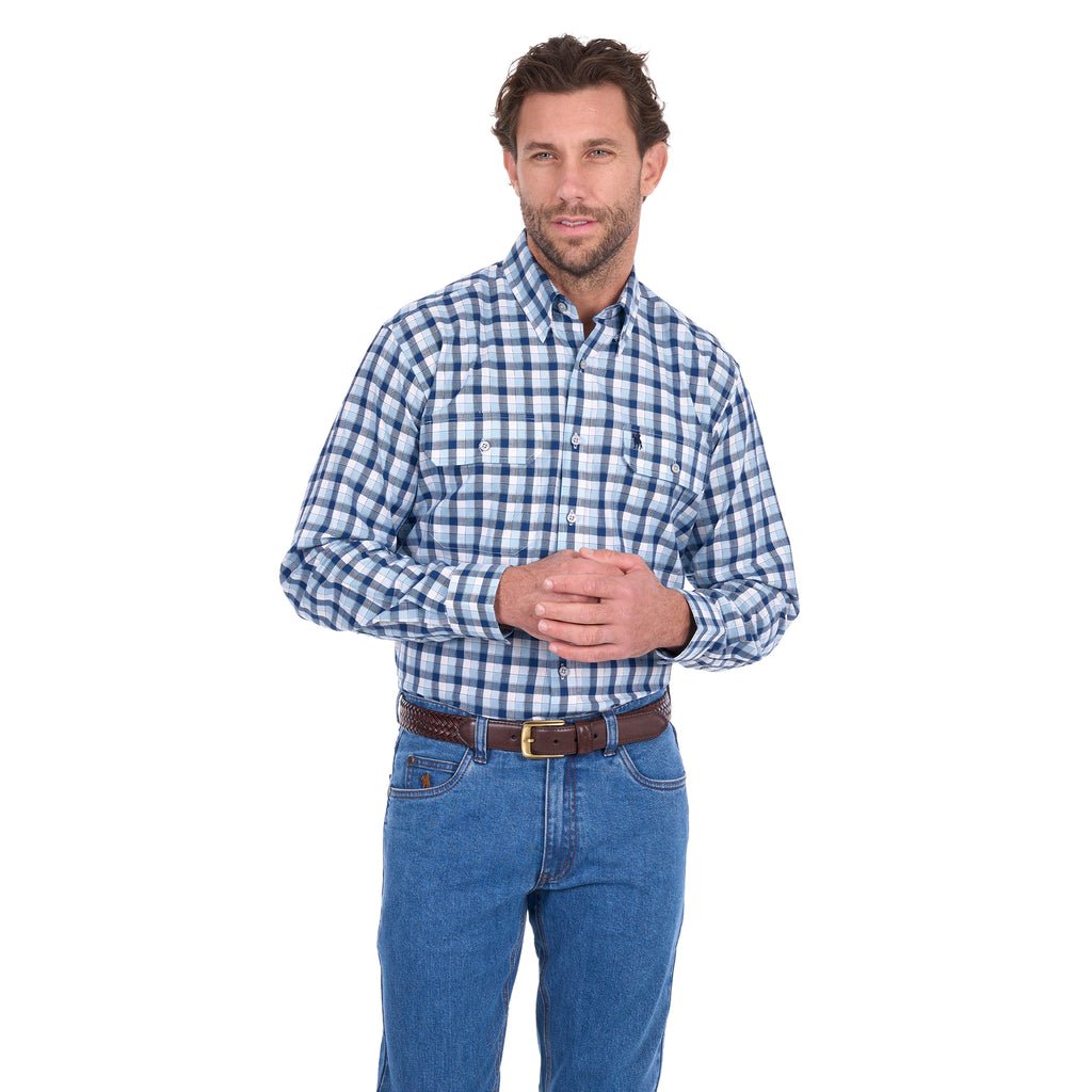A man modelling a navy, blue and white Thomas Cook Men's Mitchell Long Sleeve Shirt (TCP1115100) paired with a brown belt and denim jeans on a white background.