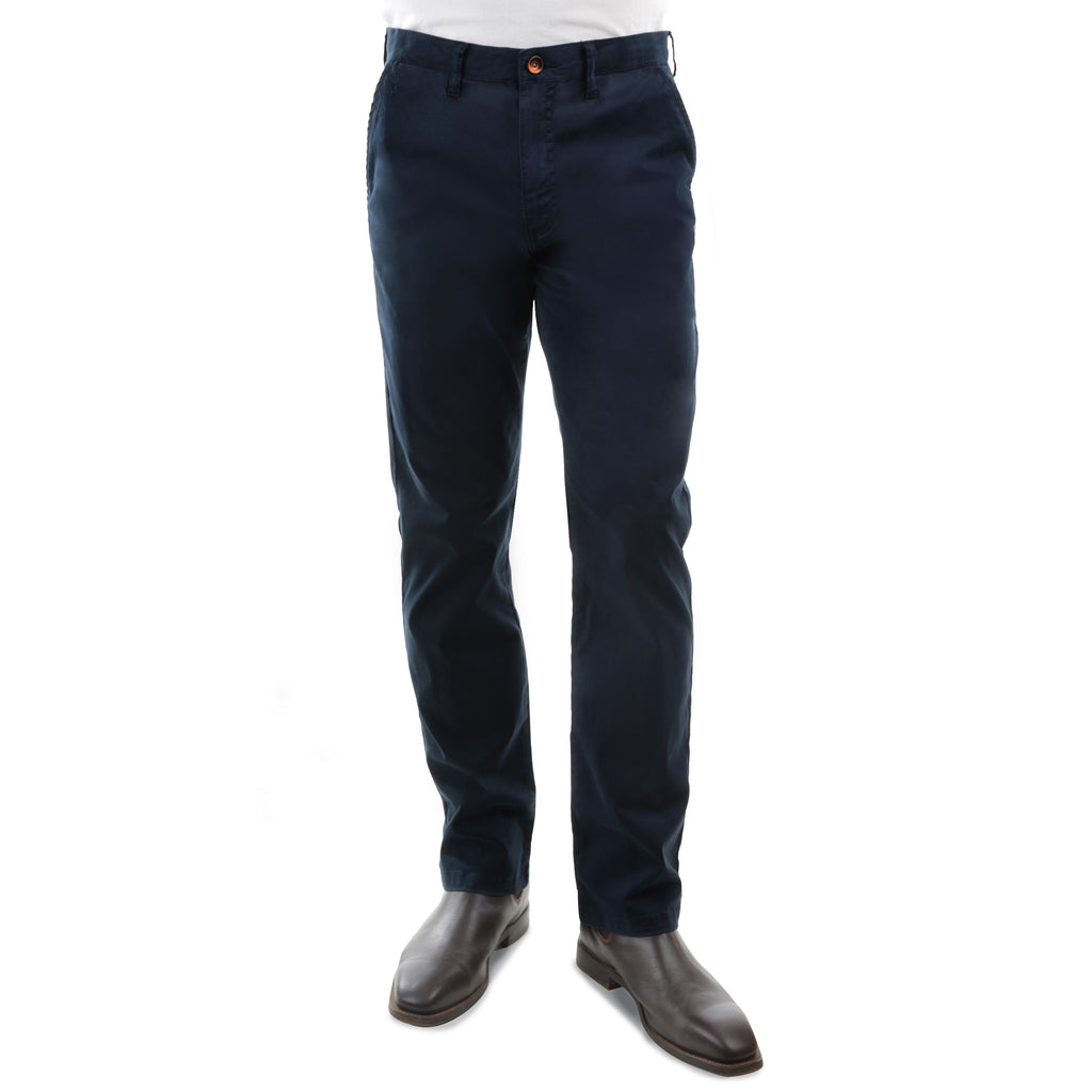 A man from the waist down wearing a pair of dark navy Thomas Cook Men's Tailored Fit Mossman Comfort Waist Trousers (TCP1209091) with a pair of brown boots on a white studio background.