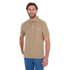 A man modelling a sand coloured Thomas Cook Men's Tailored Short Sleeve Polo (TCP1506009) paired with blue denim jeans on a white background.