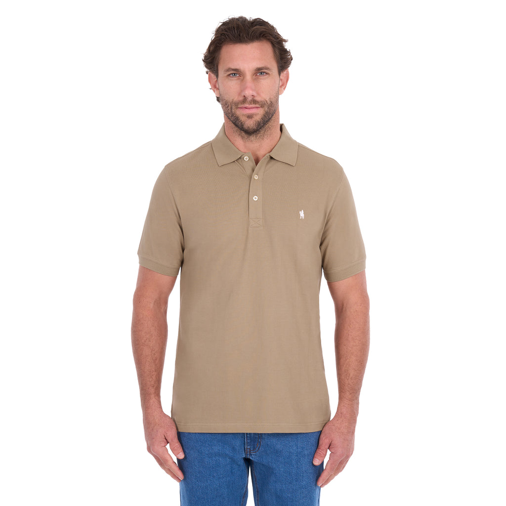 A man modelling a sand coloured Thomas Cook Men's Tailored Short Sleeve Polo (TCP1506009) paired with blue denim jeans on a white background.