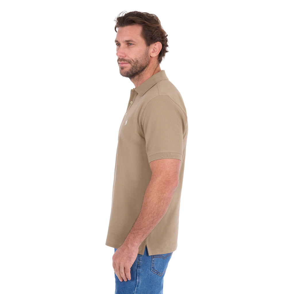 A man in profile modelling a sand coloured Thomas Cook Men's Tailored Short Sleeve Polo (TCP1506009) paired with blue denim jeans on a white background.