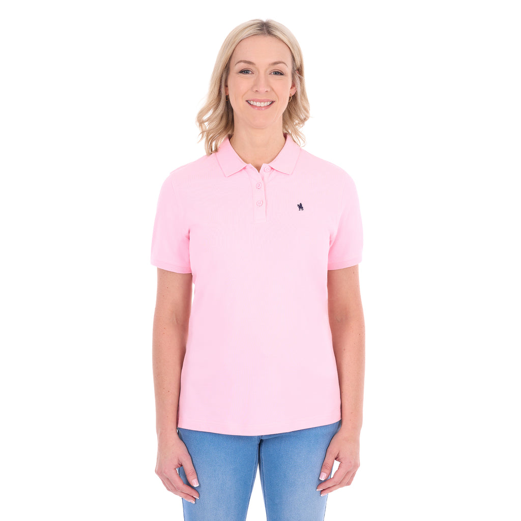 A woman modelling a light pink Thomas Cook Women's Classic Stretch Short Sleeve Polo (TCP2512059) and blue jeans, against a plain white background.