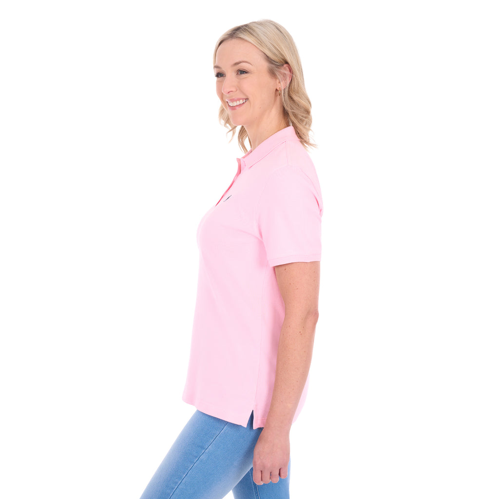 A woman modelling a light pink Thomas Cook Women's Classic Stretch Short Sleeve Polo (TCP2512059) and blue jeans, shown from a side profile against a plain white background.