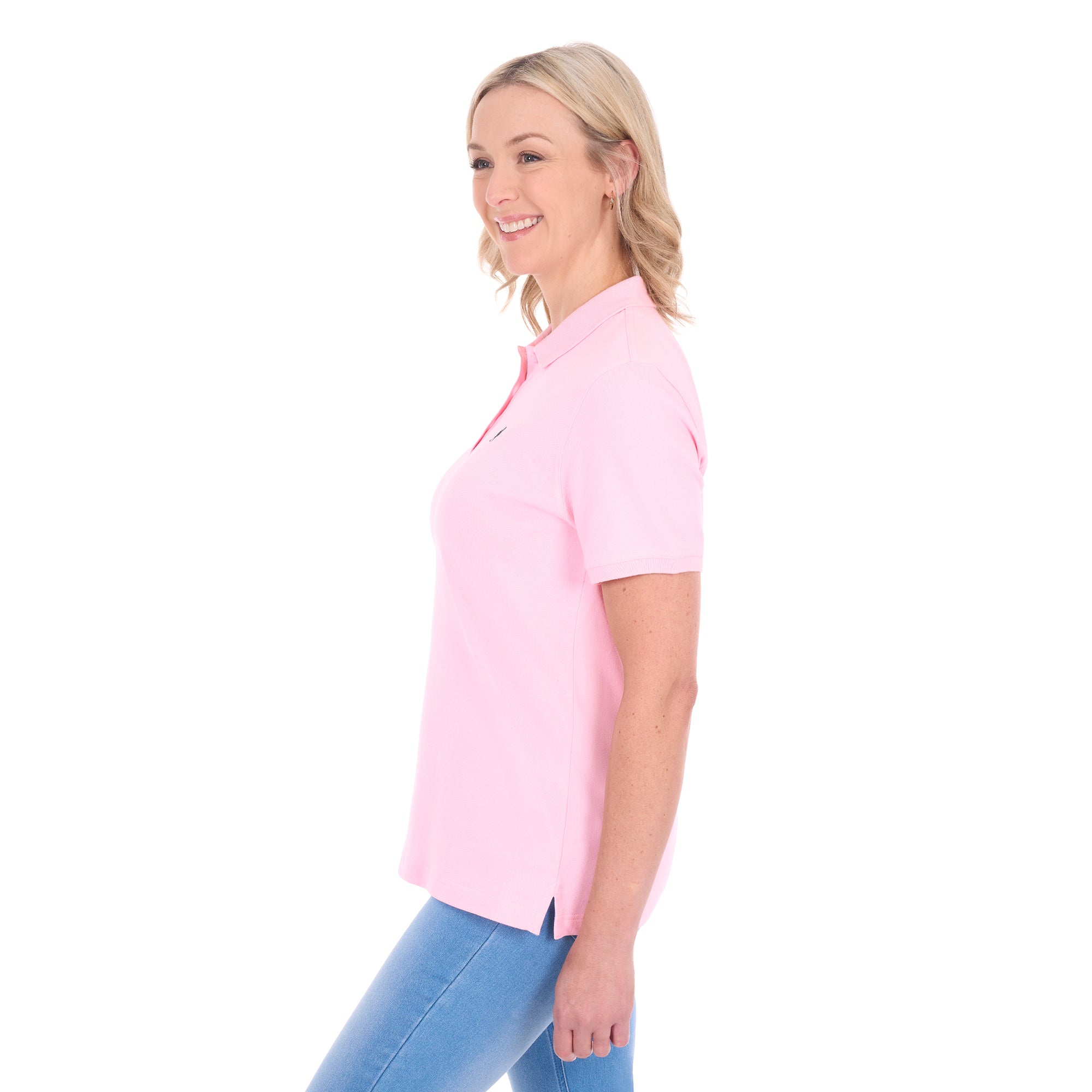 A woman modelling a light pink Thomas Cook Women's Classic Stretch Short Sleeve Polo (TCP2512059) and blue jeans, shown from a side profile against a plain white background.