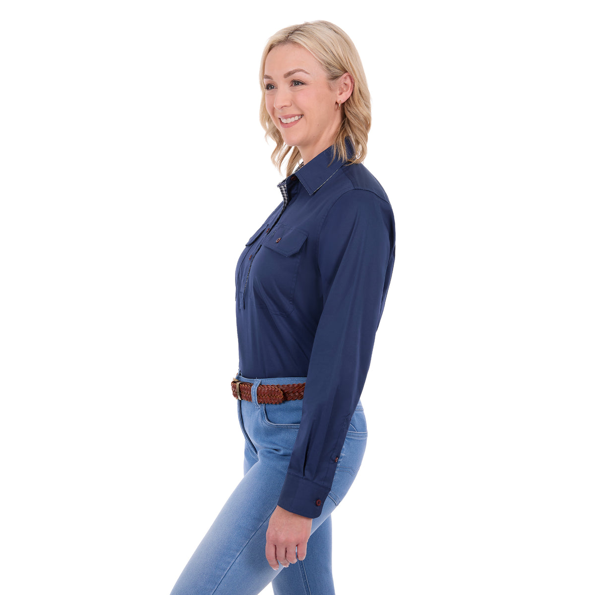 A woman in side profile, modelling a navy blue Thomas Cook Women's Stretch Drill Half Button Long Sleeve Work Shirt (TCP2100106) with two chest pockets, paired with blue jeans and a brown woven belt, against a plain white background.