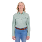 A woman modelling a mint green Thomas Cook Women's Stretch Drill Half Button Long Sleeve Work Shirt (TCP2100106) with two chest pockets, paired with blue jeans and a brown woven belt, against a plain white background.