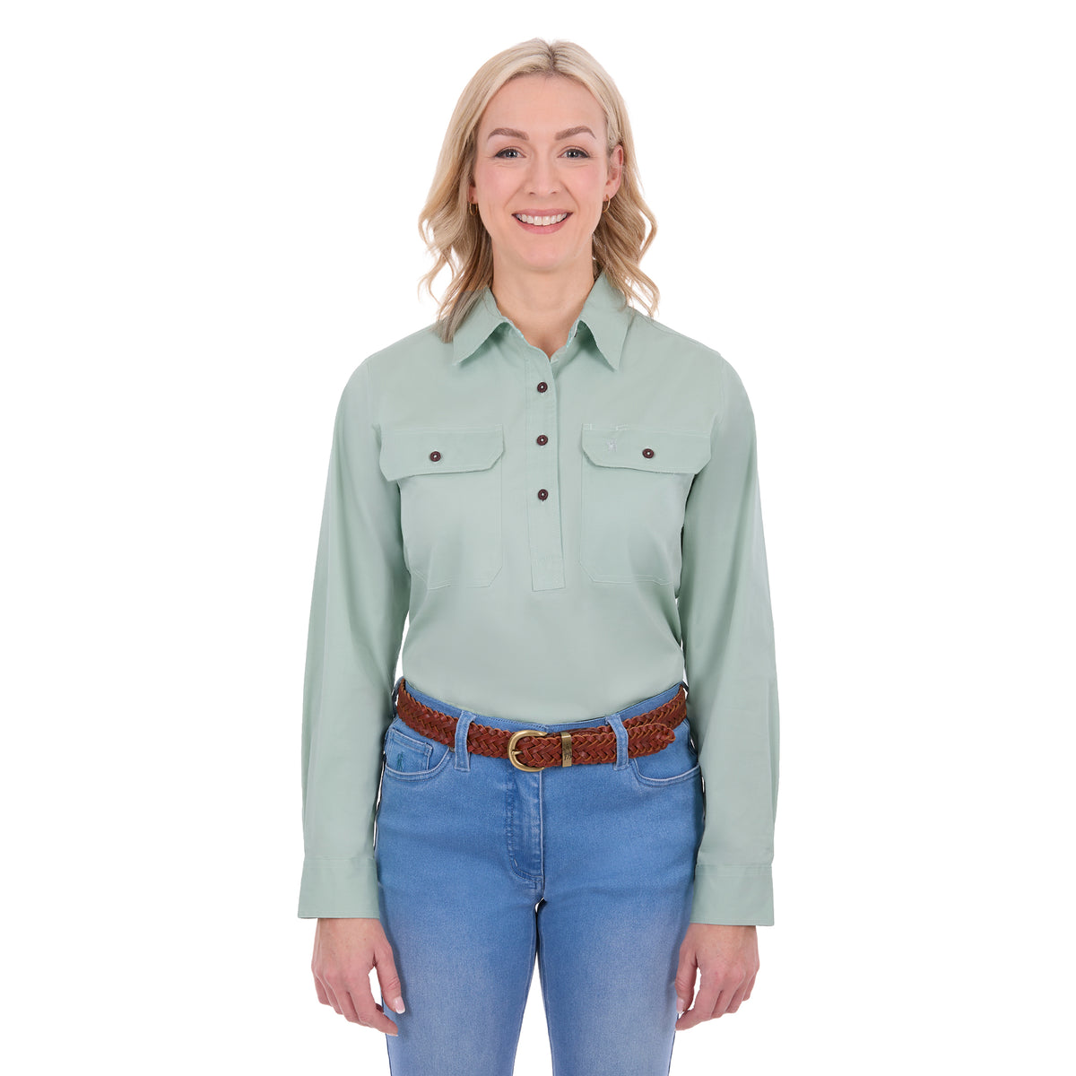 A woman modelling a mint green Thomas Cook Women's Stretch Drill Half Button Long Sleeve Work Shirt (TCP2100106) with two chest pockets, paired with blue jeans and a brown woven belt, against a plain white background.