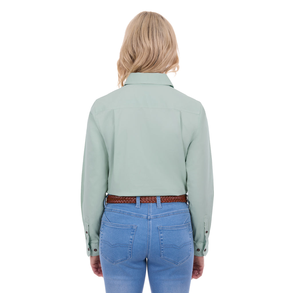 A woman from behind modelling a mint green Thomas Cook Women's Stretch Drill Half Button Long Sleeve Work Shirt (TCP2100106), paired with blue jeans and a brown woven belt, against a plain white background.