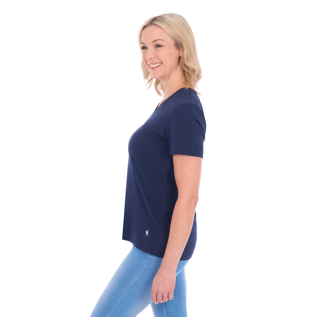 A woman in profile with blonde hair wearing a navy blue Thomas Cook Women's V Neck Short Sleeve Tee (TCP2550105) and denim jeans, standing against a plain white background.