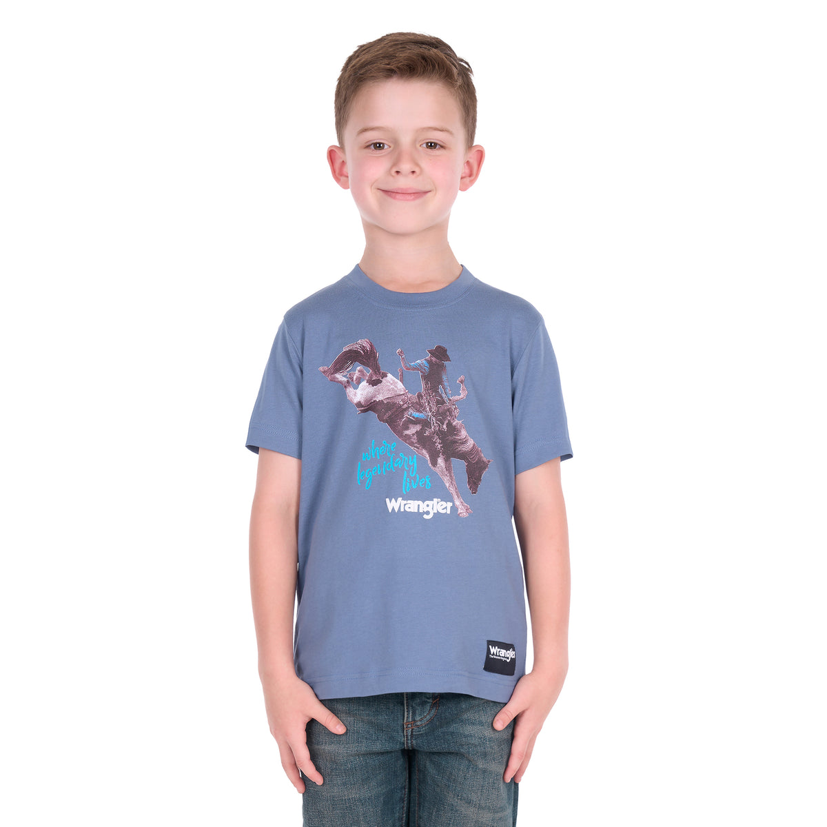 A young boy wearing a storm blue Wrangler Boys Michael Short Sleeve Tee (X6S3557684) with a cowboy graphic print, paired with blue jeans, standing against a solid white background.