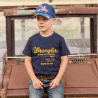 A young boy wearing a Wrangler Boys Robert Short Sleeved Tee (X6S3557687) in Navy with a pair of denim jeans, a brown belt and a Wrangler Children's Abe Trucker Cap (X6S3946CAP) in Navy Blue
