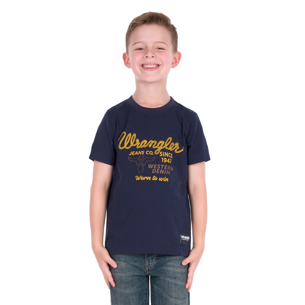 A young boy with a broad smile wearing a Wrangler Boys Robert Short Sleeved Tee (X6S3557687) in Navy with a pair of denim jeans.