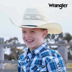 A young boy smiling outdoors while wearing a natural Wrangler Children's Boll Bangora Hat (X4Y3901BOL) and a blue and white plaid Wrangler button-down shirt. The Wrangler brand logo is visible in the top right corner.