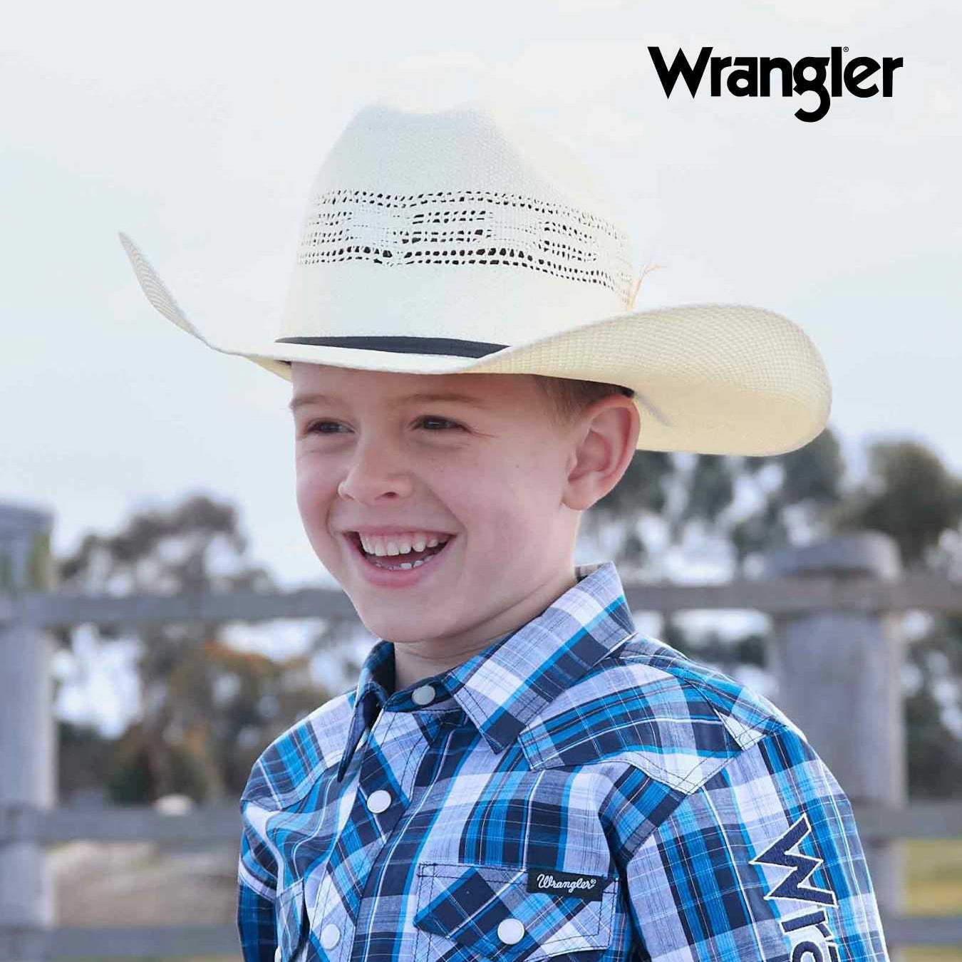 A young boy smiling outdoors while wearing a natural Wrangler Children's Boll Bangora Hat (X4Y3901BOL) and a blue and white plaid Wrangler button-down shirt. The Wrangler brand logo is visible in the top right corner.