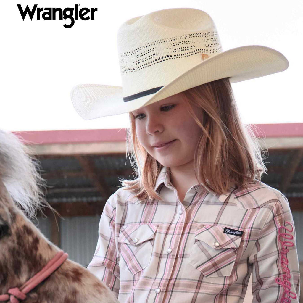 A young girl wearing a Wrangler Children's Boll Bangora Hat (X4Y3901BOL) and a pink and beige plaid shirt, standing next to a horse in a barn. The Wrangler logo is visible in the top left corner.