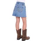 A girl shown from the back wearing a faded blue Wrangler Girls Grace Skirt (X6S5202720) with decorative stitching and brown cowboy boots, against a plain white background.