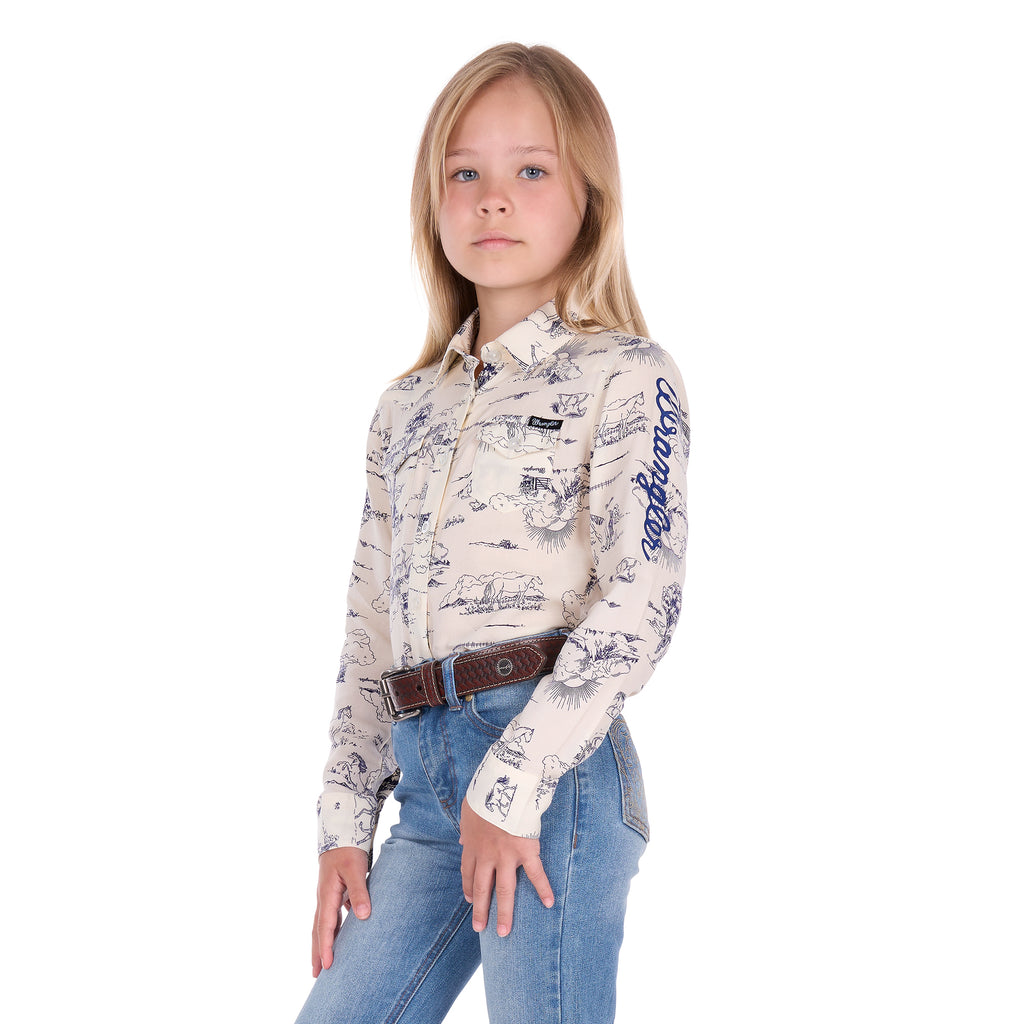 A young girl with blonde hair stands against a white background wearing a Wrangler Girls Ivory Logo Long Sleeve Shirt (X6S5127602) with a horse print on a cream base, paired with blue jeans and a dark tan Wrangler Children's Denny Belt (XCP7951BLT).