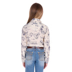 A young girl with blonde hair stands facing away from the camera against a white background wearing a Wrangler Girls Ivory Logo Long Sleeve Shirt (X6S5127602) with a horse print on a cream base, paired with blue jeans and a dark tan Wrangler Children's Denny Belt (XCP7951BLT).