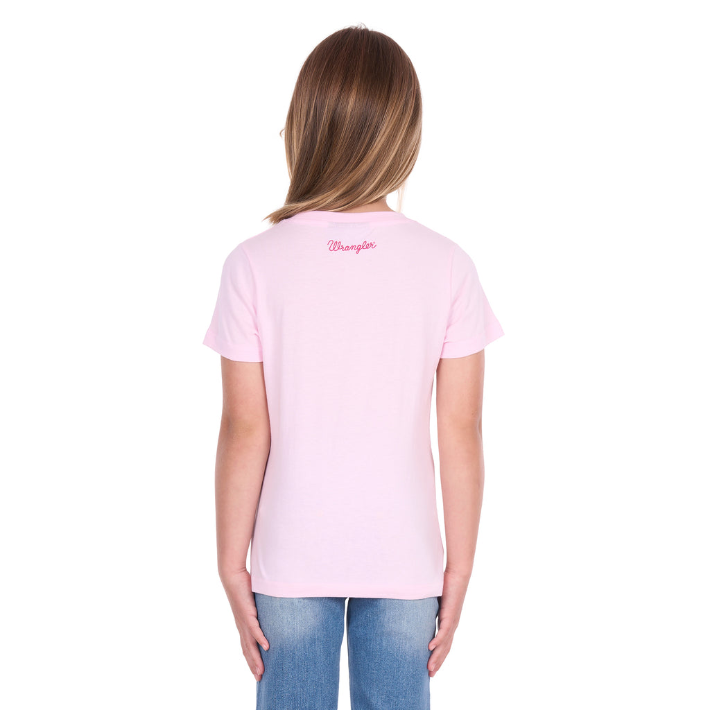 A young girl with blonde hair photographed from behind wearing a pastel pink Wrangler Girls Jenna T-Shirt (X6S5598639) with a back neck Wrangler logo and blue jeans, standing against a plain white background.