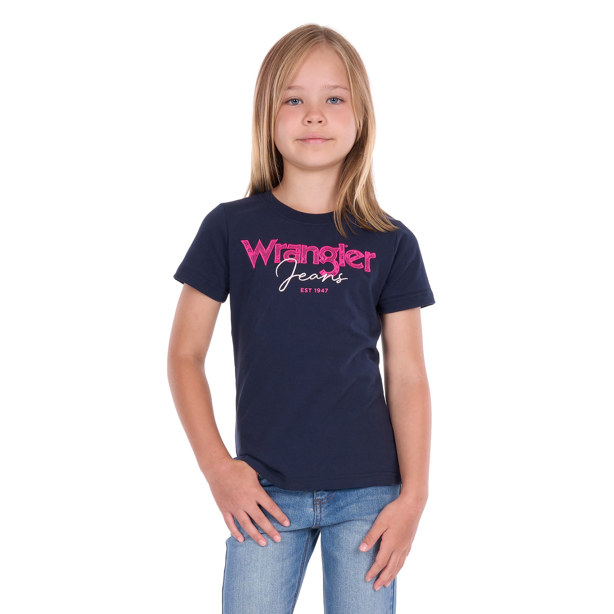 A young girl with blonde hair wearing a navy blue Wrangler Girls Maya T-Shirt (X6S5598649) and blue jeans, standing against a plain white background.