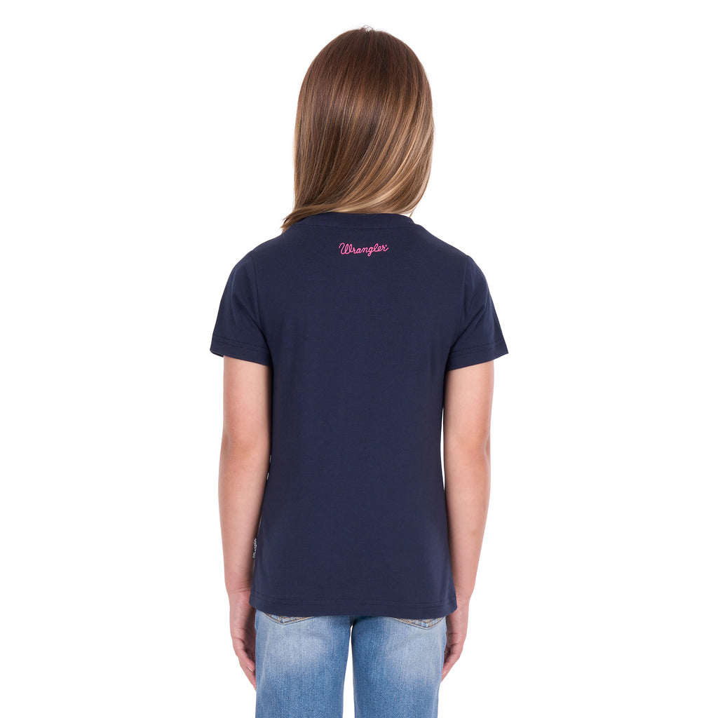 A young girl with blonde hair photographed from behind wearing a navy blue Wrangler Girls Maya T-Shirt (X6S5598649) and blue jeans, standing against a plain white background.