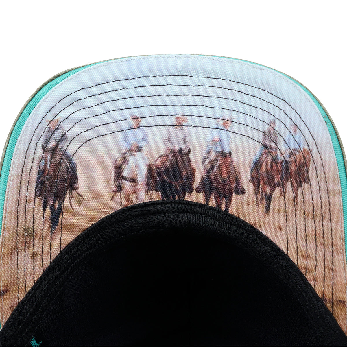 Close-up of the curved brim of the Wrangler Layton High Profile Trucker Cap (X6S1945CAP) featuring a printed western scene of five cowboys riding horses across a desert landscape, with a black curved lower band and a thin sage green edge.