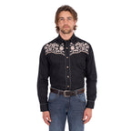 A man wearing a black Wrangler Men's Anthony Embroidered L/S Shirt (X6S1113674) Black with intricate white floral embroidery across the chest, paired with blue jeans and a brown belt, against a plain white background.