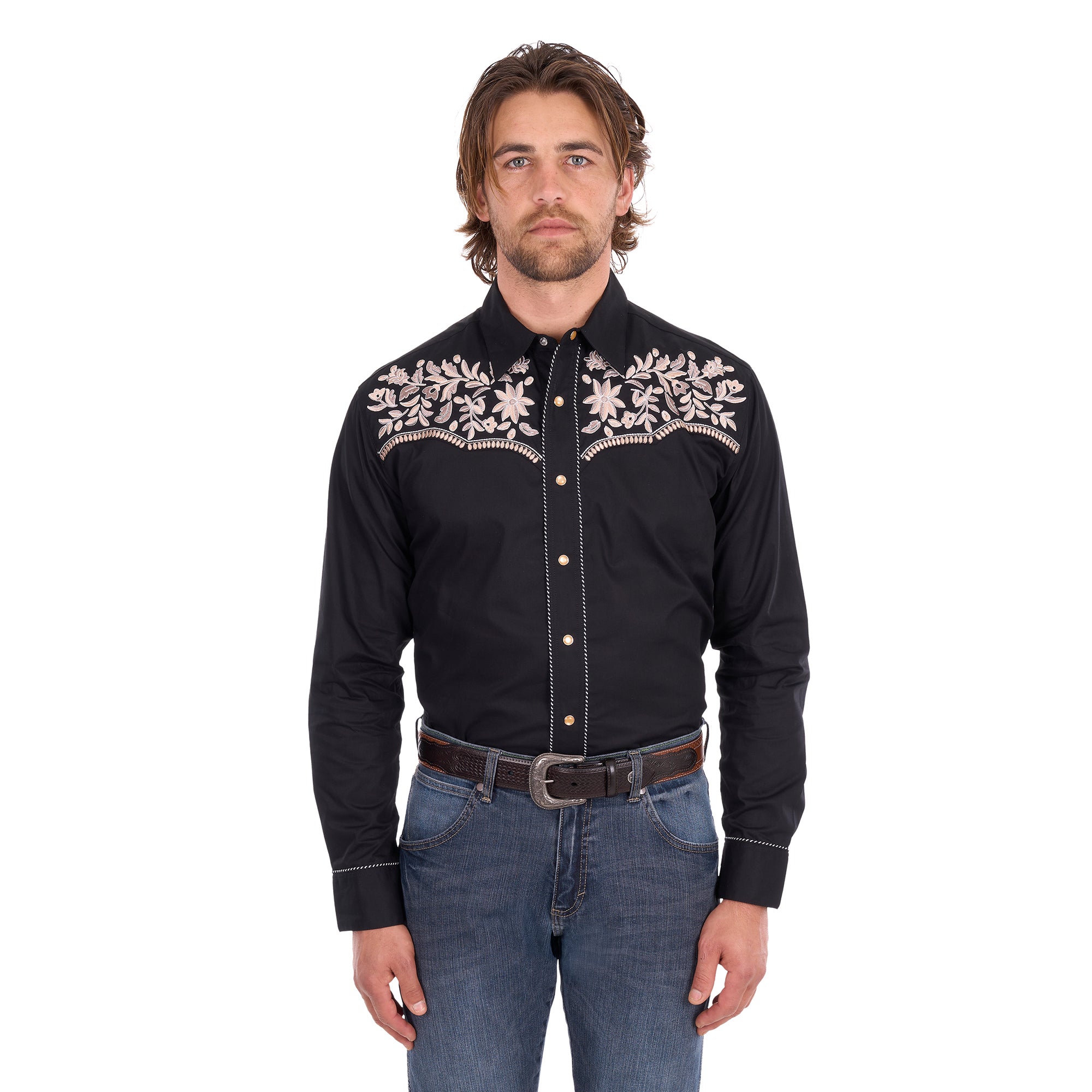 A man wearing a black Wrangler Men's Anthony Embroidered L/S Shirt (X6S1113674) Black with intricate white floral embroidery across the chest, paired with blue jeans and a brown belt, against a plain white background.