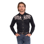 A man wearing a black Wrangler Men's Anthony Embroidered L/S Shirt (X6S1113674) Black with intricate white floral embroidery across the chest, paired with blue jeans and a brown belt, against a plain white background.